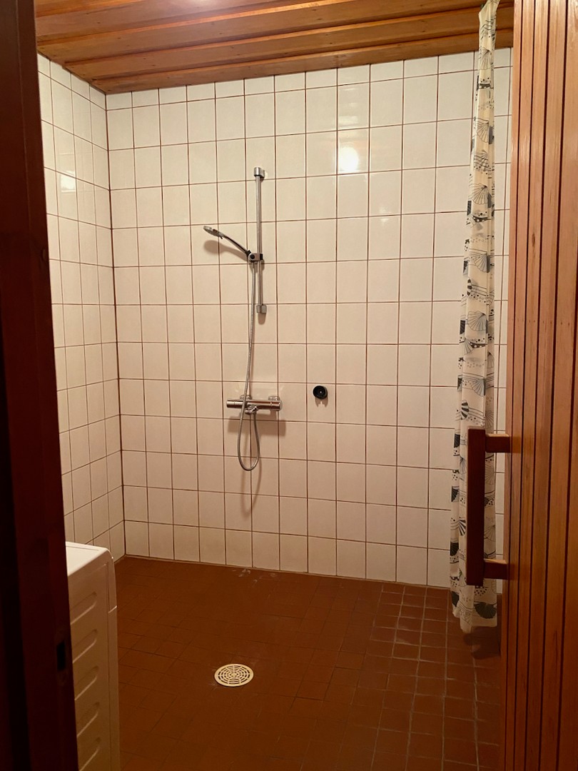 Näkymä saunasta pesuhuoneeseen, jossa on hyvin väljyyttä. Verhokisko ja suihkuverho suojaa ovea.